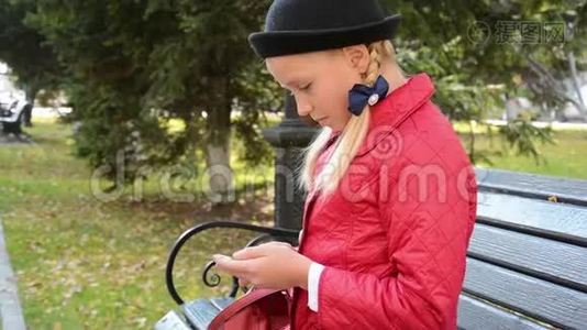 今年秋天，城市公园的一位年轻女孩在智能手机上使用应用程序坐在长椅上视频