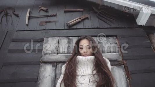 美丽的年轻女子穿着针织毛衣，在棚子边摆着工具。视频