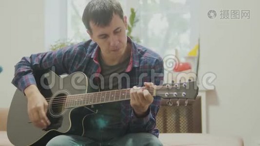 一个人演奏的吉他。 男子演奏声吉他慢动作视频。 在房间里坐在沙发上。 生活方式视频