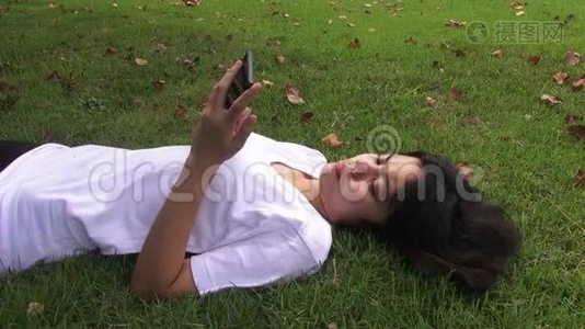 年轻女子躺在草地上发短信，在公园里发短信。视频