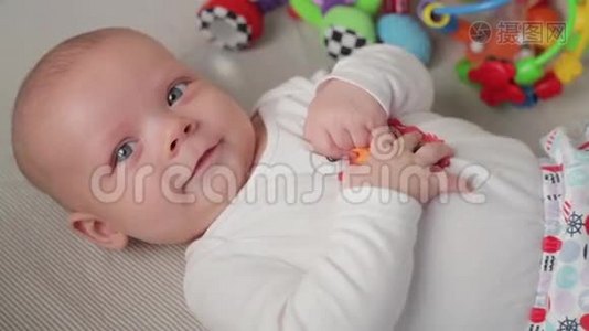 一个可爱的小宝宝正看着相机，在一张白色的床单上很开心。视频