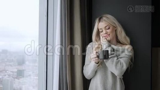 美丽的金发女人拿着陶瓷杯的茶或咖啡享受。 在床上喝茶。 看着窗户喝茶视频
