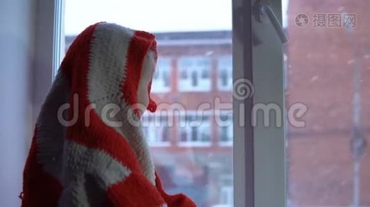 小可爱的女孩坐在窗台上，望着外面的雪城风景。视频