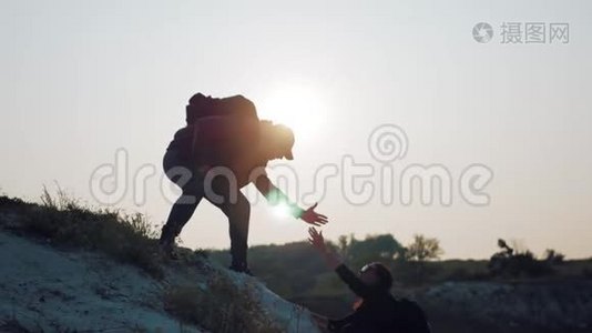 在两个登山者之间帮忙的剪影。 两个徒步旅行者在山顶上，一个人帮助一个人攀登一个纯粹的视频