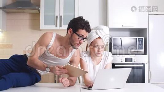 年轻的商务夫妇在家厨房里用笔记本电脑工作。视频