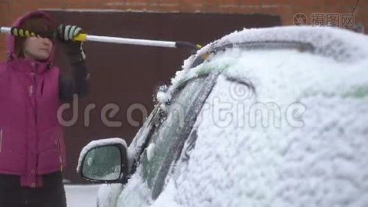 年轻女子在车上擦雪和冰。 冬季暴风雪视频
