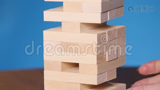 年轻人的手在蓝色背景上玩jenga，特写。 一个人在玩jenga的时候建造了一座积木塔视频