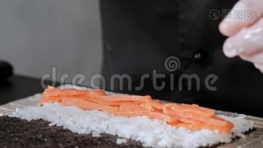 年轻的男性寿司厨师准备日本寿司卷的米饭，鲑鱼，鳄梨和诺里。 餐厅厨房。视频