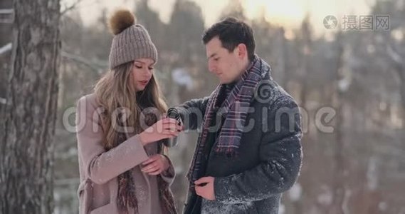 快乐的一对夫妇捧着热茶杯在冬天的风景。 年轻的情侣在寒假里，站在一个视频