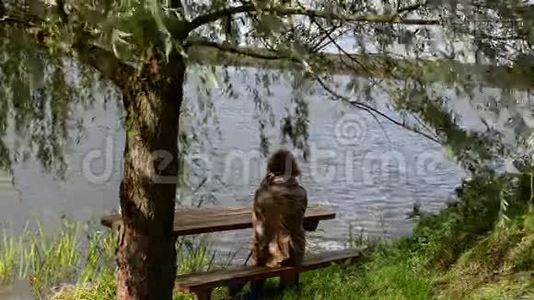 女子坐木凳柳树动风湖放松视频