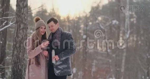 快乐的一对夫妇捧着热茶杯在冬天的风景。 年轻的情侣在寒假里，站在一个视频