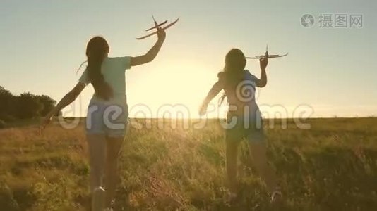 快乐的童年概念。 飞行的梦想。 两个女孩在日落时玩玩具飞机。 以太阳为背景的儿童视频