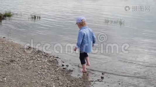 小男孩沿着河走。 那孩子在湖边跑。 慢动作。 快乐的婴儿在水边玩耍。视频