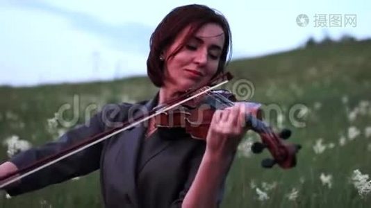 黄昏时分，女小提琴手在草地上拉小提琴.视频
