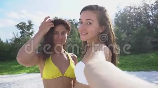 两个年轻漂亮的女孩在海滩上摆姿势拍照。视频