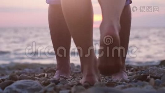在美丽的夕阳下，一对情侣在海边约会时的腿。 男人举起手来视频
