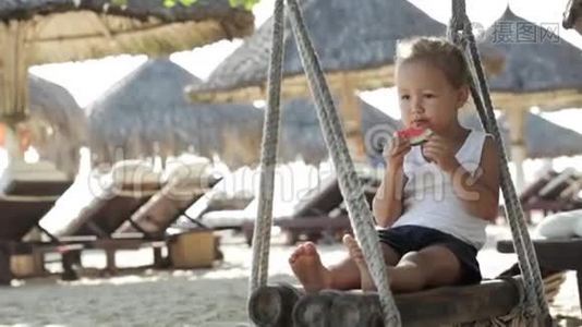 小可爱的小女孩坐在秋千上，在沙滩上吃红色的西瓜视频