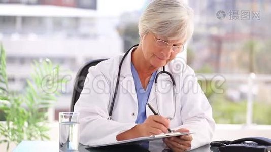 严重成熟的医生在剪贴板上写字视频