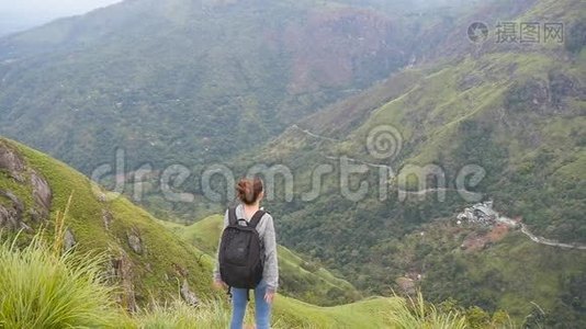 年轻的女徒步旅行者，背包伸向山顶，举起双手。 女游客站在视频