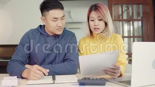 年轻的亚洲夫妇管理财务，在现代家庭使用笔记本电脑和计算器审查他们的银行账户。视频