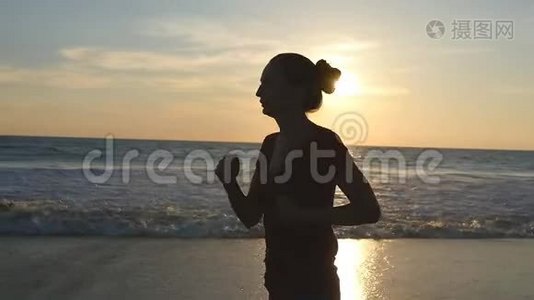 日落时在海边奔跑的年轻女子剪影。 日出时沿着海岸慢跑的女孩。 女性视频