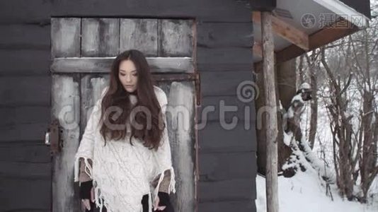 年轻的黑发女人穿着针织毛衣站在木屋旁。视频