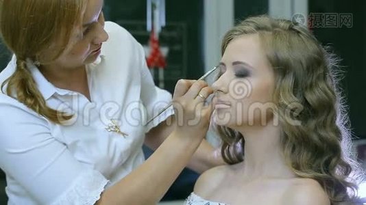 专业化妆师将色调粉涂在金发模特眼皮上做眼影。视频