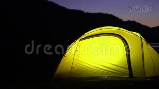 黄色帐篷在山湖畔花费.. 晚安。 在帐篷里，光线燃烧。视频
