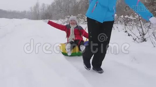 快乐的童年概念。 家庭寒假。 孩子和母亲在雪地里雪橇。 女儿和妈妈在冬天玩视频