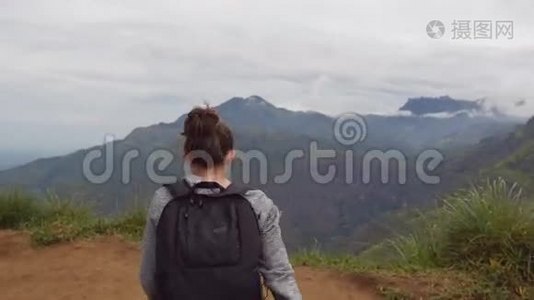 年轻的女徒步旅行者，背包伸向山顶，举起双手。 女游客站在视频