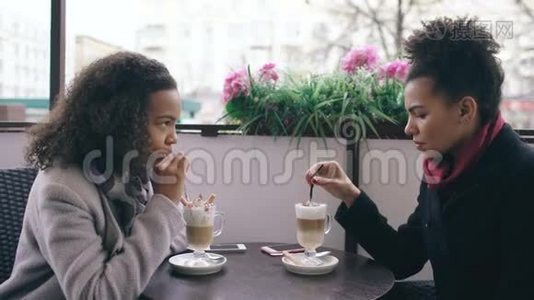 两个迷人的混血女人在街头咖啡馆里聊天喝咖啡。 朋友参观商场后玩得开心视频