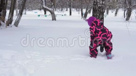 一个穿着粉红色冬季连衣裙的小女孩玩雪。视频