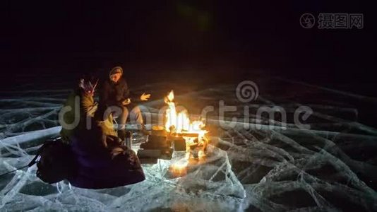 夜间有三个乘火的旅行者在冰上。 在冰上露营。 帐篷就在火旁边。 贝加尔湖。 就在附近视频
