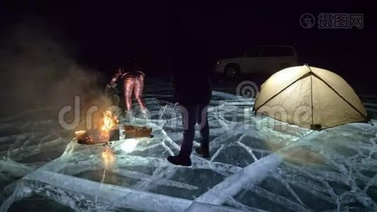夜间有三个乘火的旅行者在冰上。 在冰上露营。 帐篷就在火旁边。 贝加尔湖。 就在附近视频