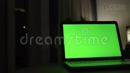 带有绿色屏幕的笔记本电脑。 黑暗的家庭办公室。视频