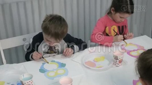 孩子们，男孩和女孩在教室里围着桌子坐在一起画画。视频