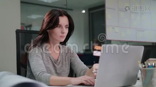一位女士坐在办公室里用笔记本电脑工作视频