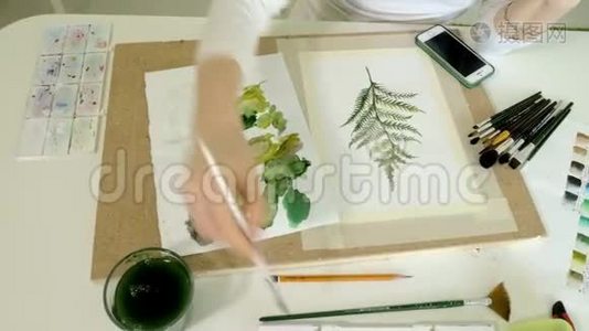 坐在桌旁，一个红发的小美女用颜料和画笔作画视频