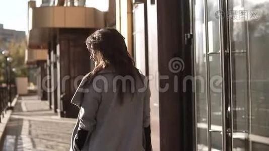 迷人的年轻女子穿着外套，微笑着穿过秋天的城市。 现代社会背景下的可爱女孩视频