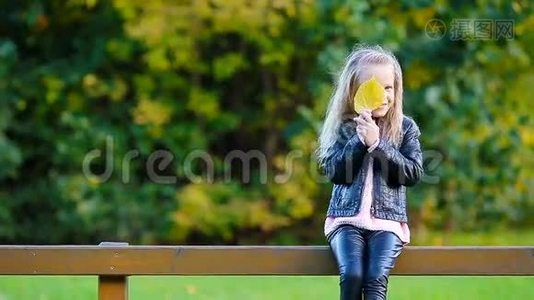美丽的秋日，可爱的小女孩带着黄叶在户外的肖像视频