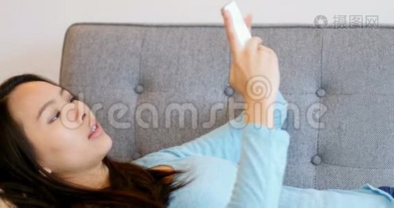 美丽的女人在沙发上放松，用手机视频