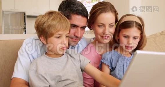 幸福的年轻家庭一起坐在沙发上用笔记本电脑视频