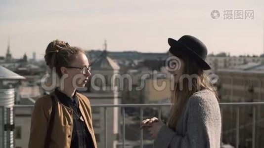 两个幸福的女人在城市全景、屋顶的背景下交谈。 在阳光明媚的日子里，朋友们在市中心散步。视频