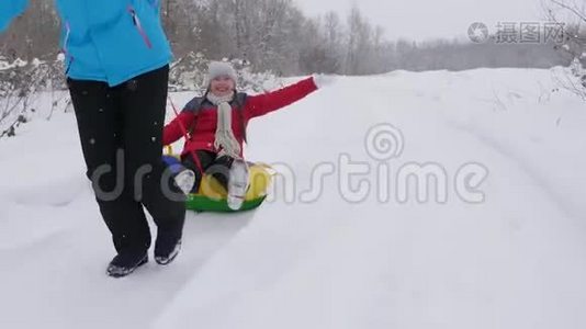 快乐的童年概念。 家庭寒假。 孩子和母亲在雪地里雪橇。 女儿和妈妈在冬天玩视频