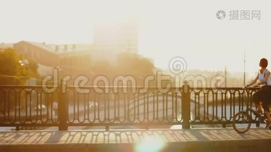 年轻女子骑自行车骑在城市桥上，背景是金色的阳光视频