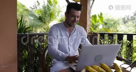 喜笑颜开的人在露台上使用笔记本电脑，偶然的商人在电脑打字外门上工作视频