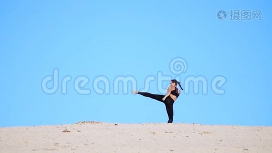 运动女孩穿着黑色的上衣和腿，练习踢腿，踢脚，和影子打架，训练打架。 在一个视频