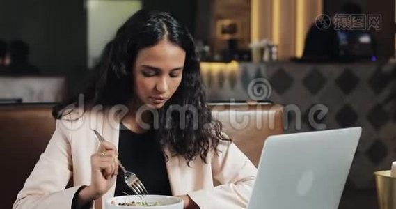商务女性坐在咖啡馆里，拿着笔记本电脑吃晚饭，桌上放着一杯茶。 上班吃午饭视频