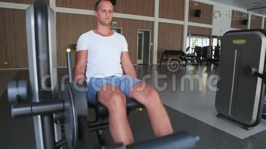 在健身房里，男人专注于训练机器上的腿视频