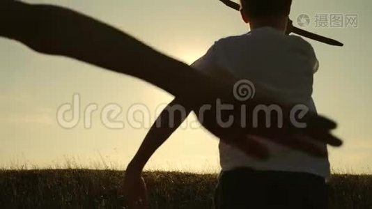 两个男孩在日落时玩一架木飞机。 孩子们玩飞机的剪影。 飞行的梦想。 儿童视频